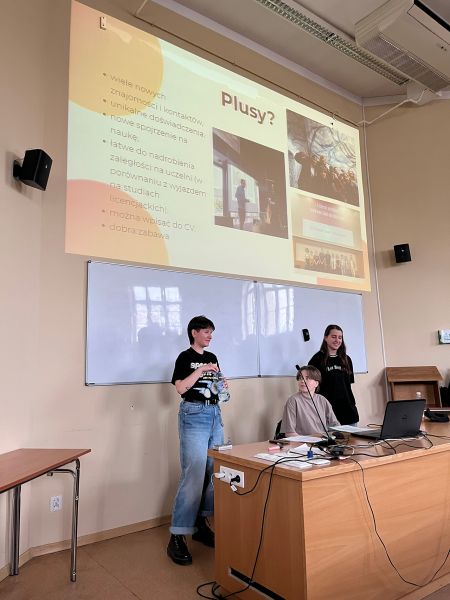 zdjęcie: trzy osoby na tle prezentacji multimedialnej z tekstem: „Plusy?”