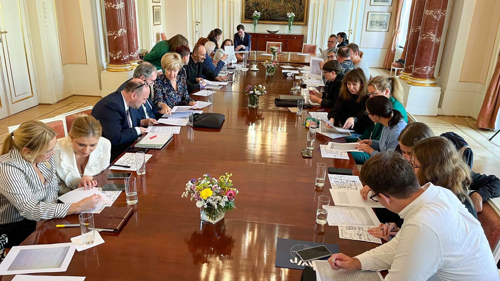 Grupa osób przy dużym stole pochylona nad kartkami papieru