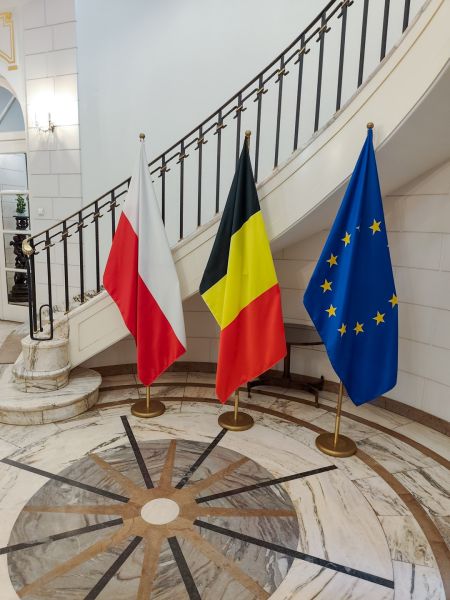 Flagi: Polski, Belgii i Unii Europejskiej na tle zabytkowych schodów