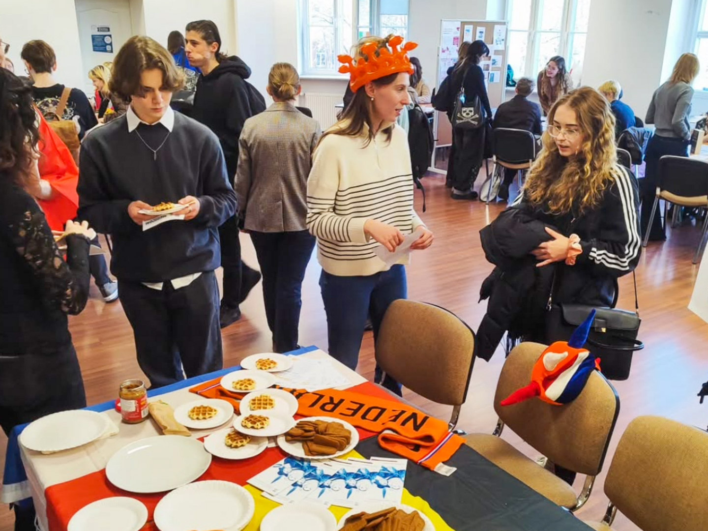 zdjęcie: grupa osób w sali seminaryjnej, stół z ulotkami, tacami z waflami i innymi przekąskami