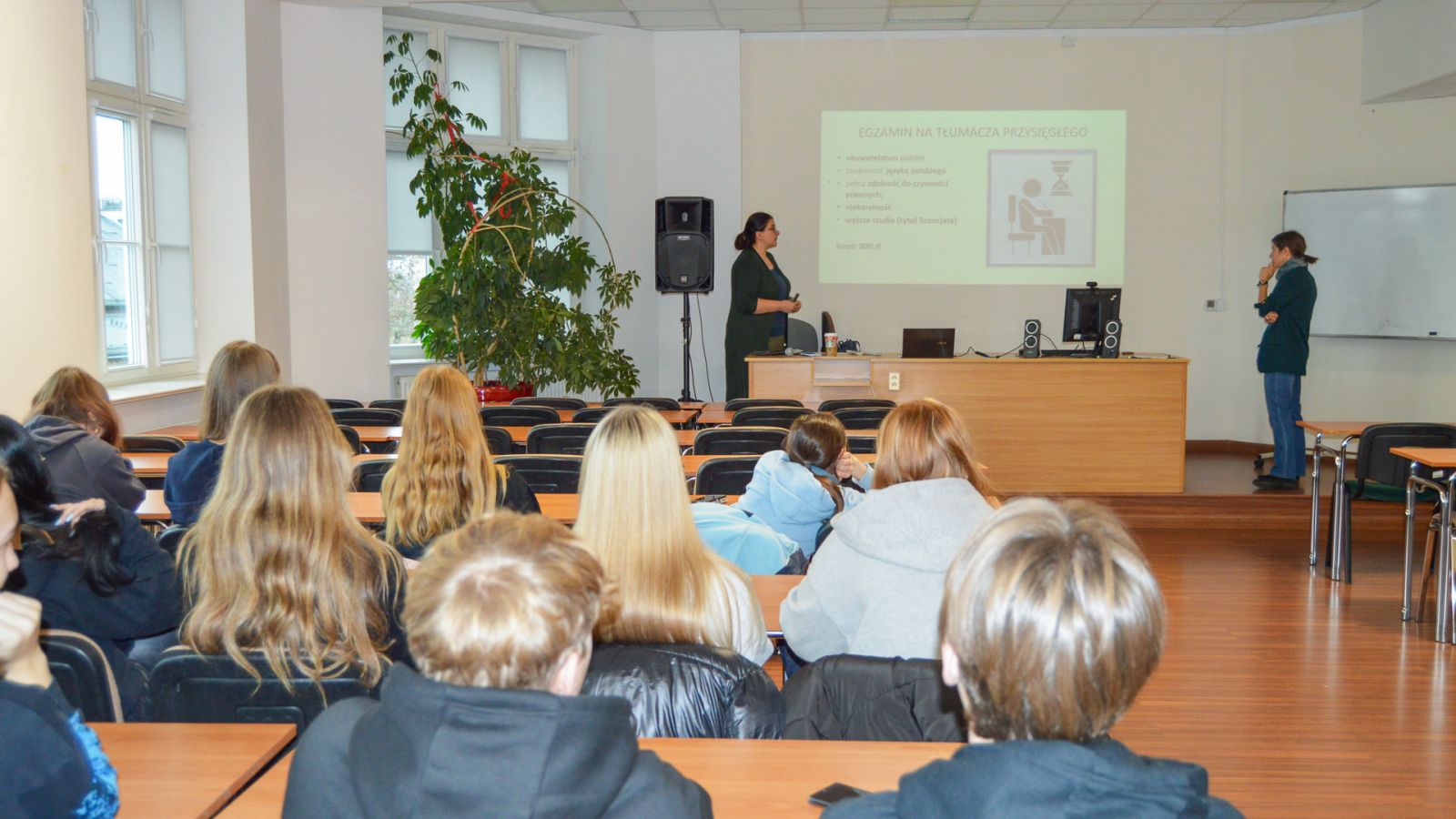 zdjęcie: dwie prowadzące warsztat lub wykład oraz publiczność w sali seminaryjnej, w tle ekran z obrazem z rzutnika