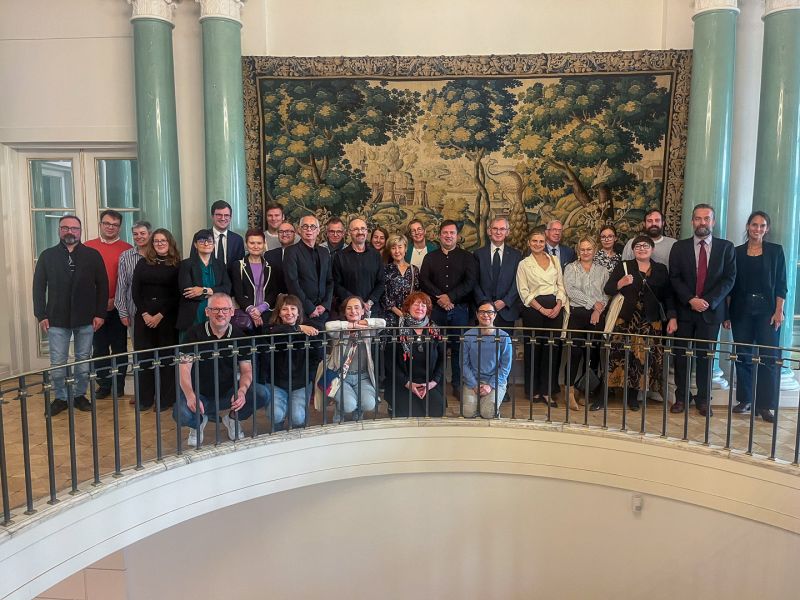 Duża grupa osób na tle zabytkowego arrasu