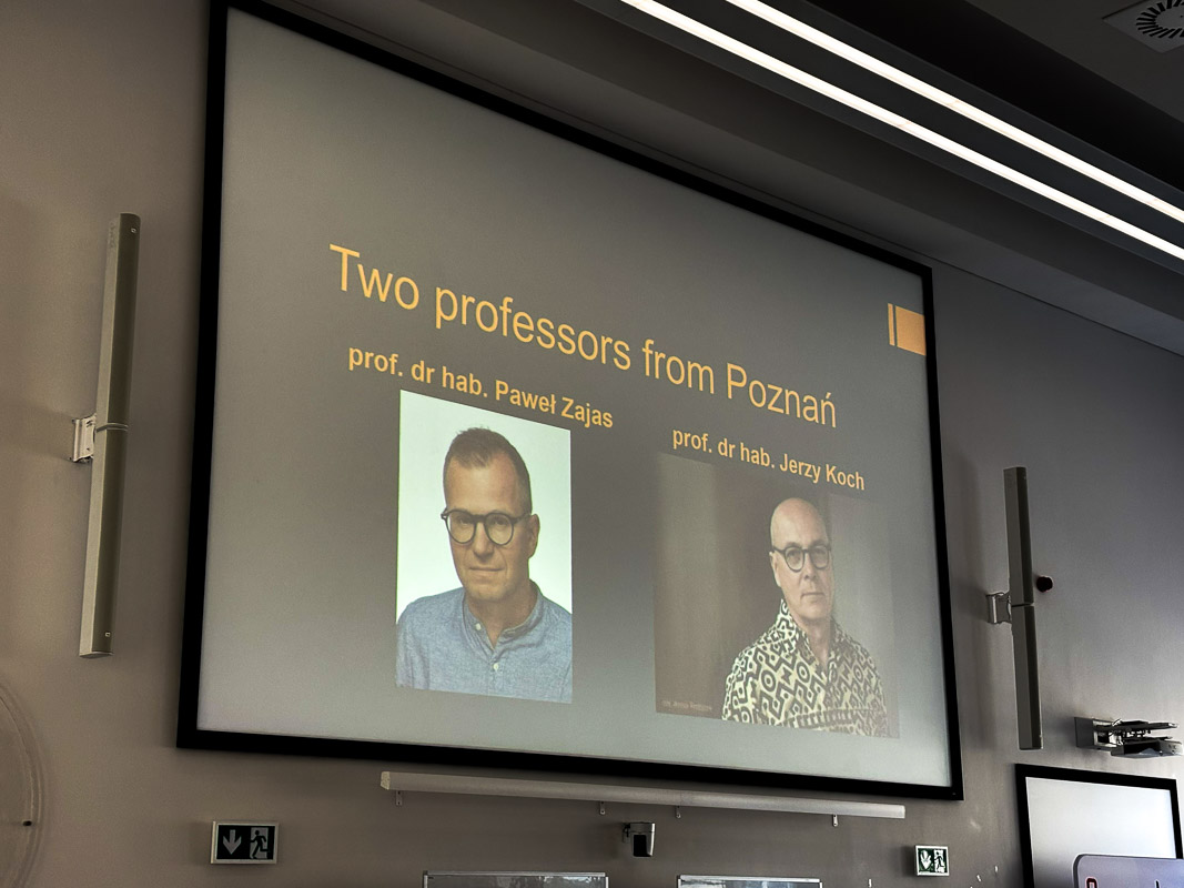 Slajd w auli przedstawia tytuł ‘Two professors from Poznań’ oraz zdjęcia dwóch wykładowców z podpisami ich imion i nazwisk (od lewej do prawej: Paweł Zajas i Jerzy Koch).