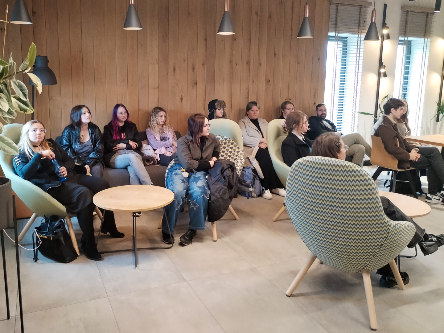 zdjęcie: grupa osób siedzi w sali, słuchając kogoś, kto znajduje się poza kadrem