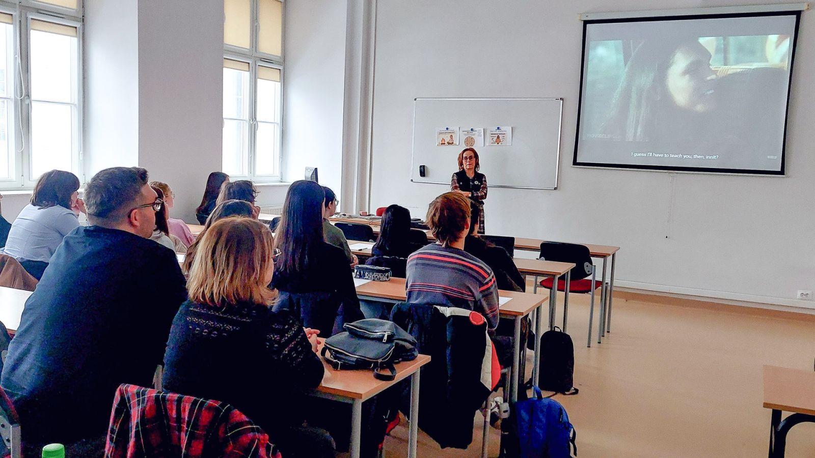 zdjęcie: osoba stoi w sali seminaryjnej; na ekranie za nią: obraz z rzutnika; przed nią: zgromadzona w sali publiczność