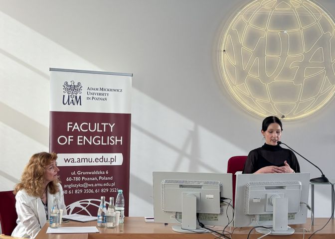 zdjęcie: sala wykładowa: za mównicą stoi osoba przemawiająca do mikrofonu; przy lewej krawędzi kadru, obok stołu siedzi druga osoba