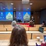 photograph: two persons stand in a lecture hall; behind them: an image projected on a screen from a beamer; in front of them: the audience