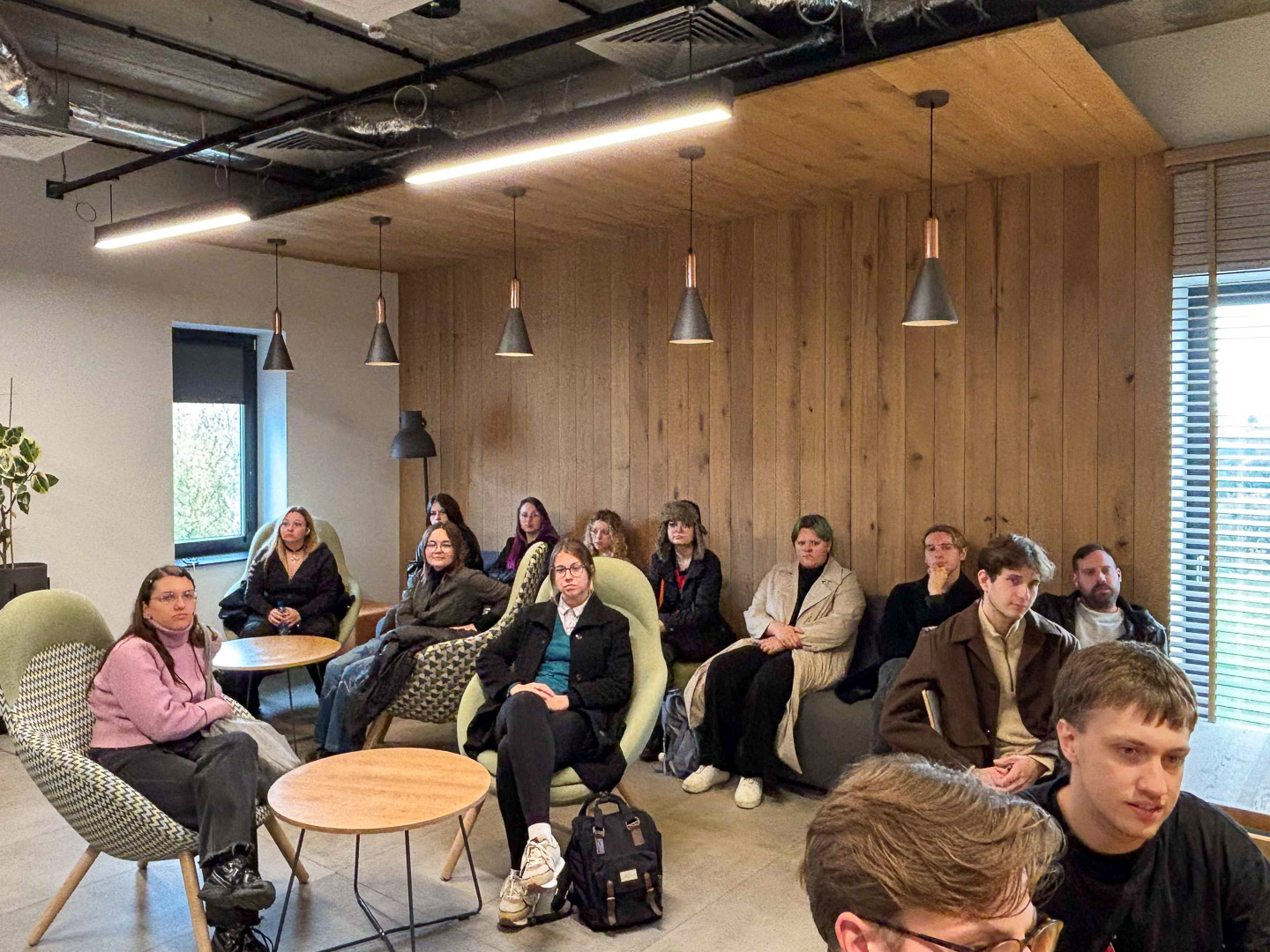 zdjęcie: grupa osób siedzi w sali, słuchając kogoś, kto znajduje się poza kadrem