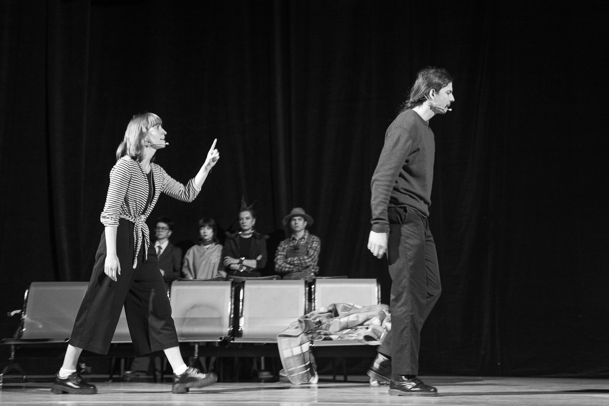photograph: six people on a stage in a theatre during a rehearsal; four are standing, two are pacing