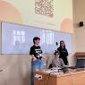 zdjęcie: trzy osoby na tle prezentacji multimedialnej z tekstem „Nasze pytania do Was” i kodem QR