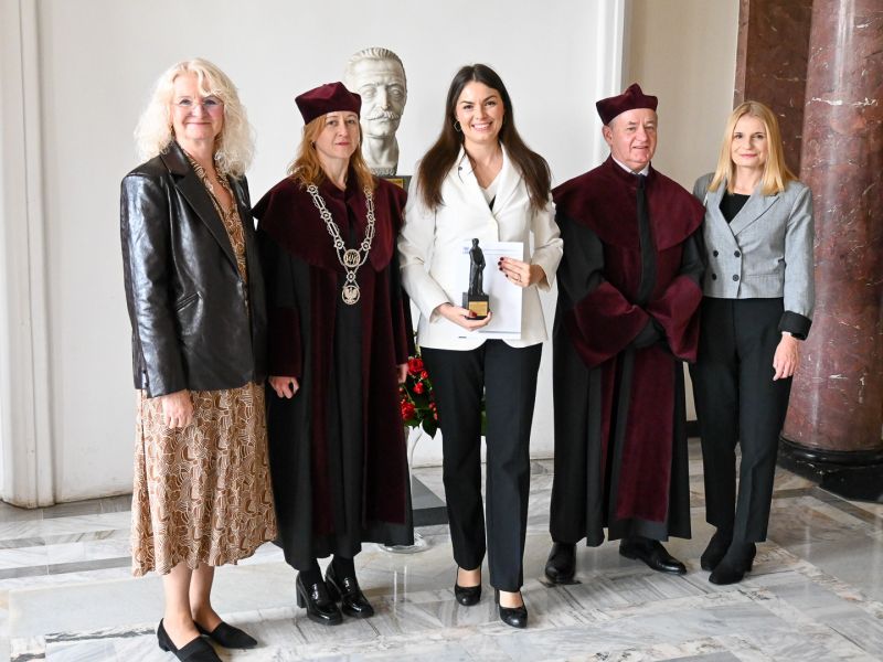 photograph: five persons pose for a photograph, one of them holding a diploma and a statuette
