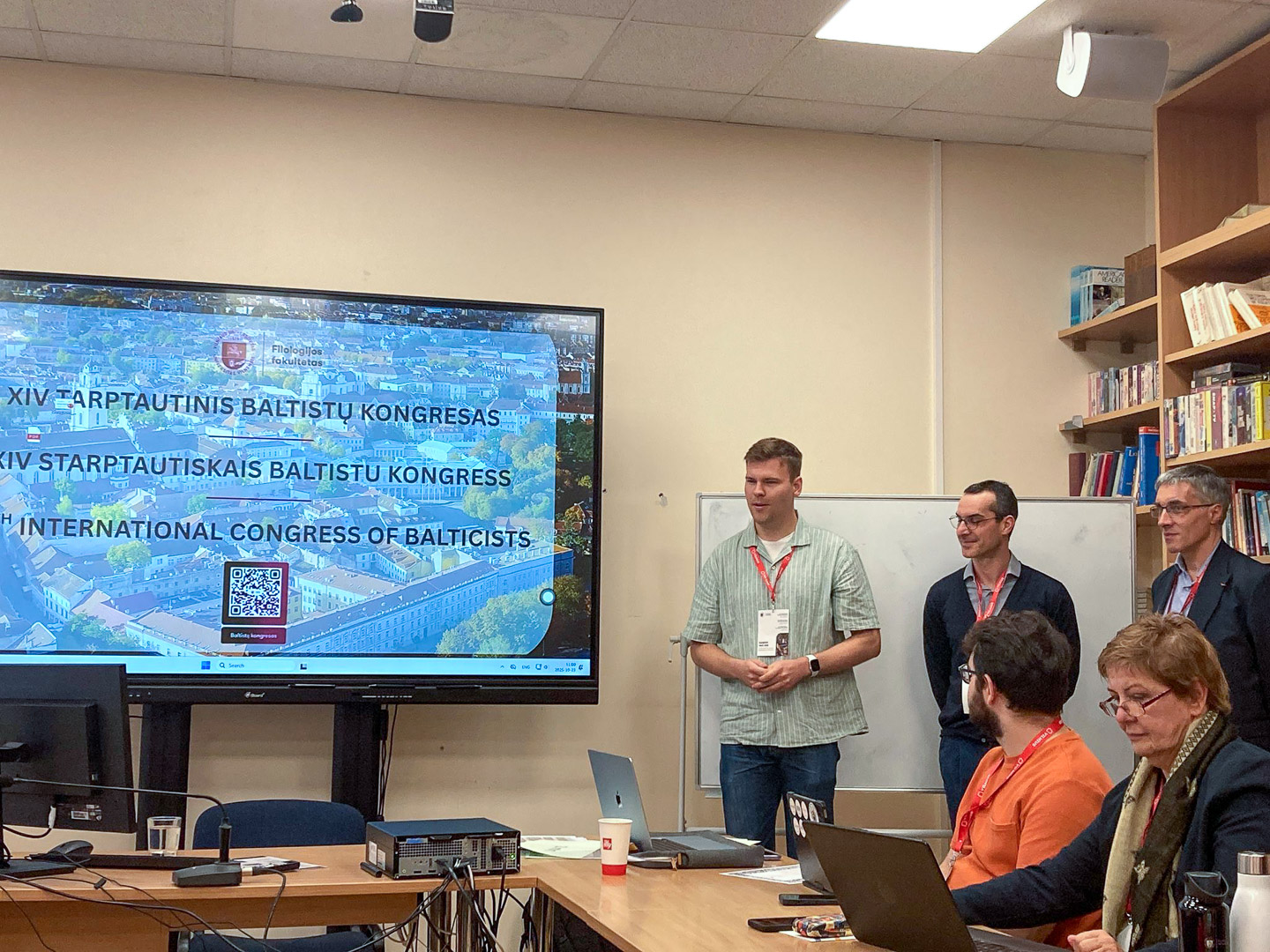 photograph: five people in a seminar room; a screen next to them displays a welcome page with the caption {14th International Congress of Balticists}