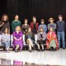 photograph: fourteen people pose on a stage in a theatre; nine are standing, five are sitting
