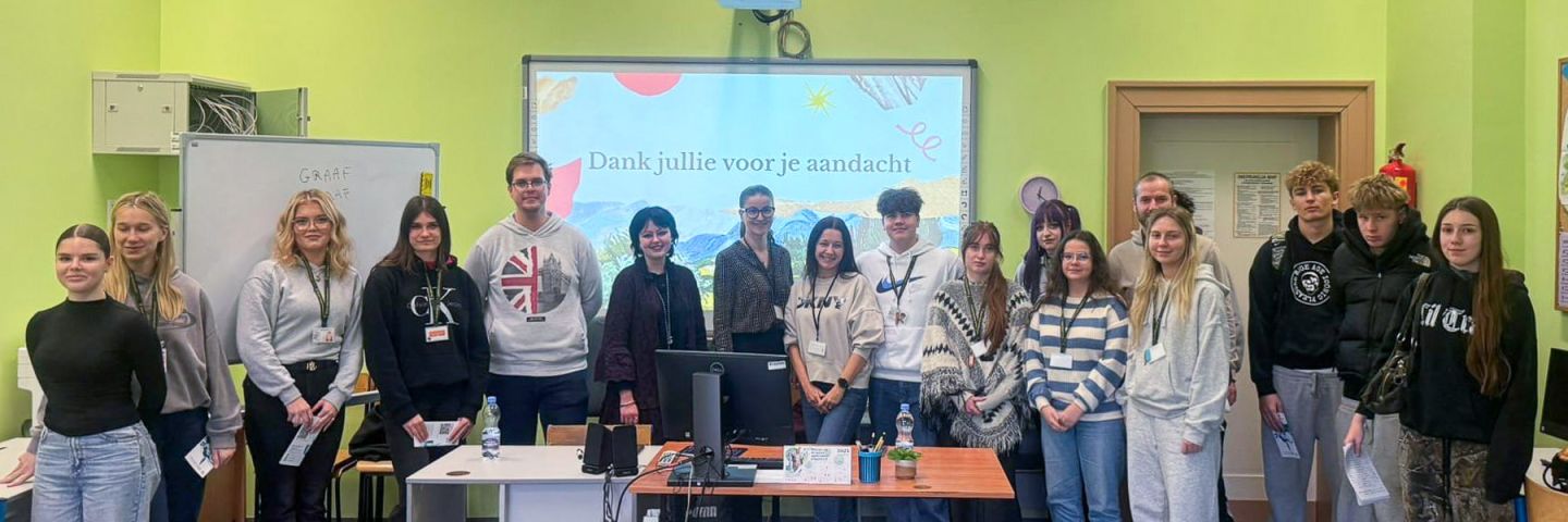 zdjęcie: grupa kilkunastu osób pozuje w sali zajęciowej; na tablicy multimedialnej za nimi slajd z napisem w języku niderlandzkim {Dank jullie voor je aandacht}