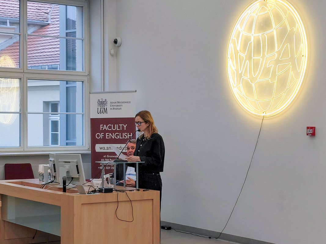 zdjęcie: jedna osoba stoi, druga siedzi za mównicą w sali wykładowej