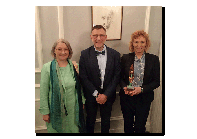 photograph: three persons facing the camera; one of them is holding a statuette