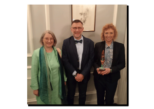 photograph: three persons facing the camera; one of them is holding a statuette