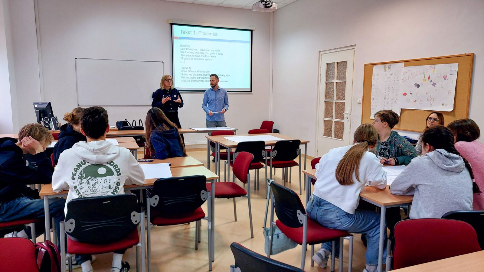 zdjęcie: dwie osoby stoją w sali seminaryjnej; na ekranie za nimi: obraz z rzutnika; przed nimi: zgromadzona w sali publiczność