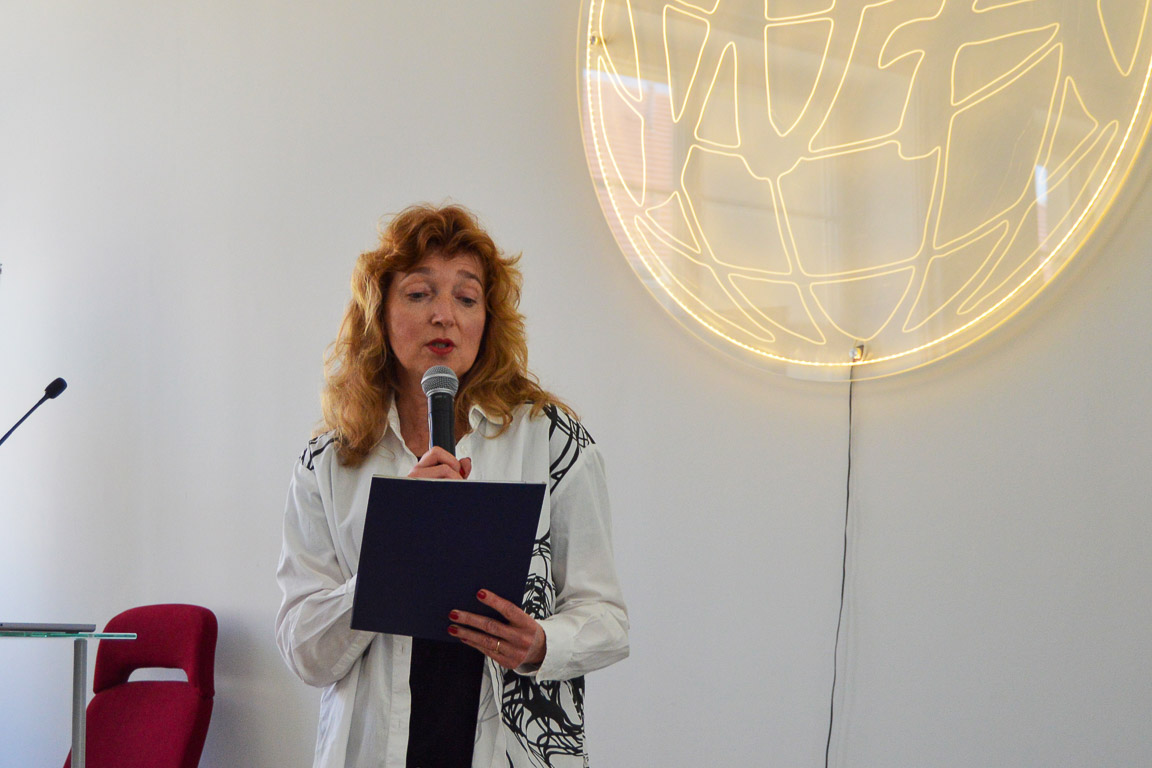 photograph: person with a microphone in hand addresses the audience (who are out of frame)