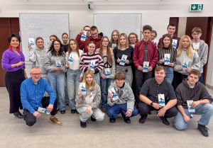 Grupa uczniów i uczennic pozujących w sali wykładowej, trzymających w rękach ulotki.