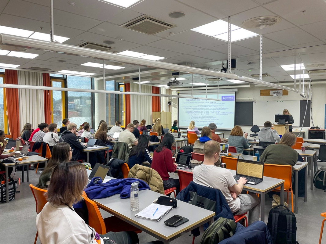zdjęcie: około dwudziestu osób w sali seminaryjnej, siedzą przy biurkach; jedna osoba stoi za mównicą; w tle ekran ze slajdem z przentacji multimedialnej