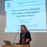 photograph: Prof. Magdalena Wrembel behind the pulpit in a seminar room; on the screen behind her is the title slide of the slide show