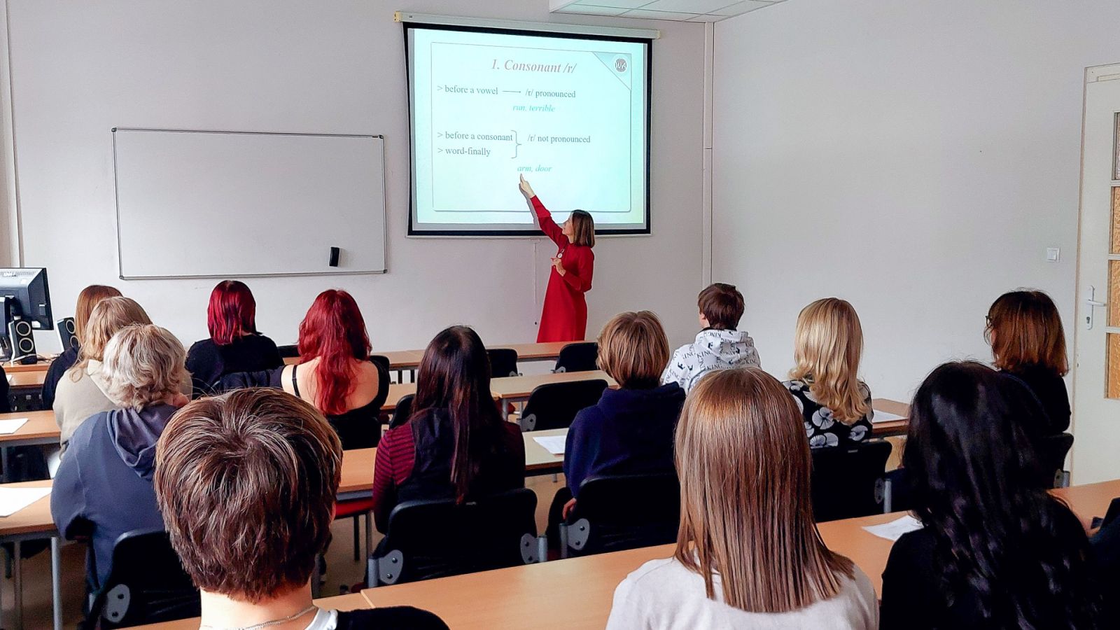 zdjęcie: osoba stoi w sali seminaryjnej; na ekranie za nią: obraz z rzutnika; przed nią: zgromadzona w sali publiczność