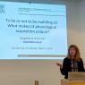 photograph: Prof. Magdalena Wrembel behind the pulpit in a seminar room; on the screen behind her is the title slide of the slide show