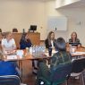 zdjęcie: grupa kilkunastu osób dyskutuje, siedząc wokół połączonych jeden z drugim stołów w sali seminaryjnej