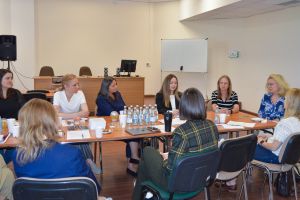 zdjęcie: grupa kilkunastu osób dyskutuje, siedząc wokół połączonych jeden z drugim stołów w sali seminaryjnej