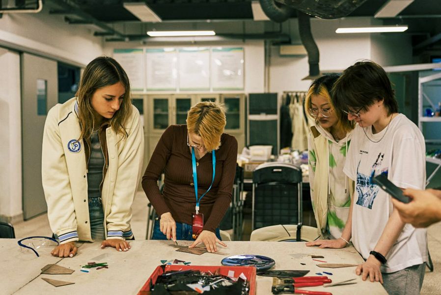 photograph: four people stand by a desk with materials for making glass jewelry