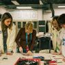 photograph: four people stand by a desk with materials for making glass jewelry