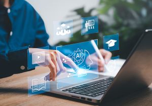 zdjęcie z elementem grafiki: osoba siedzy przy biurku, na którym jest otwarty laptop; nałożona na zdjęcie grafika sugeruje, że na ekranie wyświetlane są takie obrazy-symbole, jak: książka, odtwaracz multimedialny, grupa osób w biretach, osoba przy tablicy stojąca przed grupą słuchaczy, biret, tarcza ze strzałą z łuku wbitą w sam środek oraz koło zębate z wpisanym {AI}