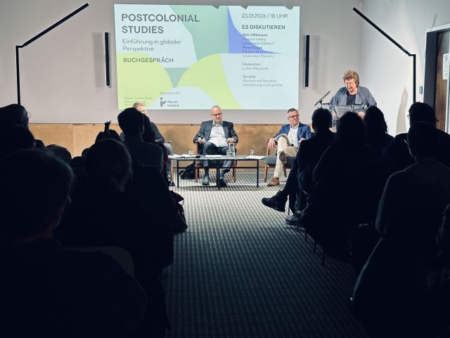 zdjęcie: publiczność słucha panelu dyskusyjnego o książce „Postcolonial Studies” prezentowanej na ekranie