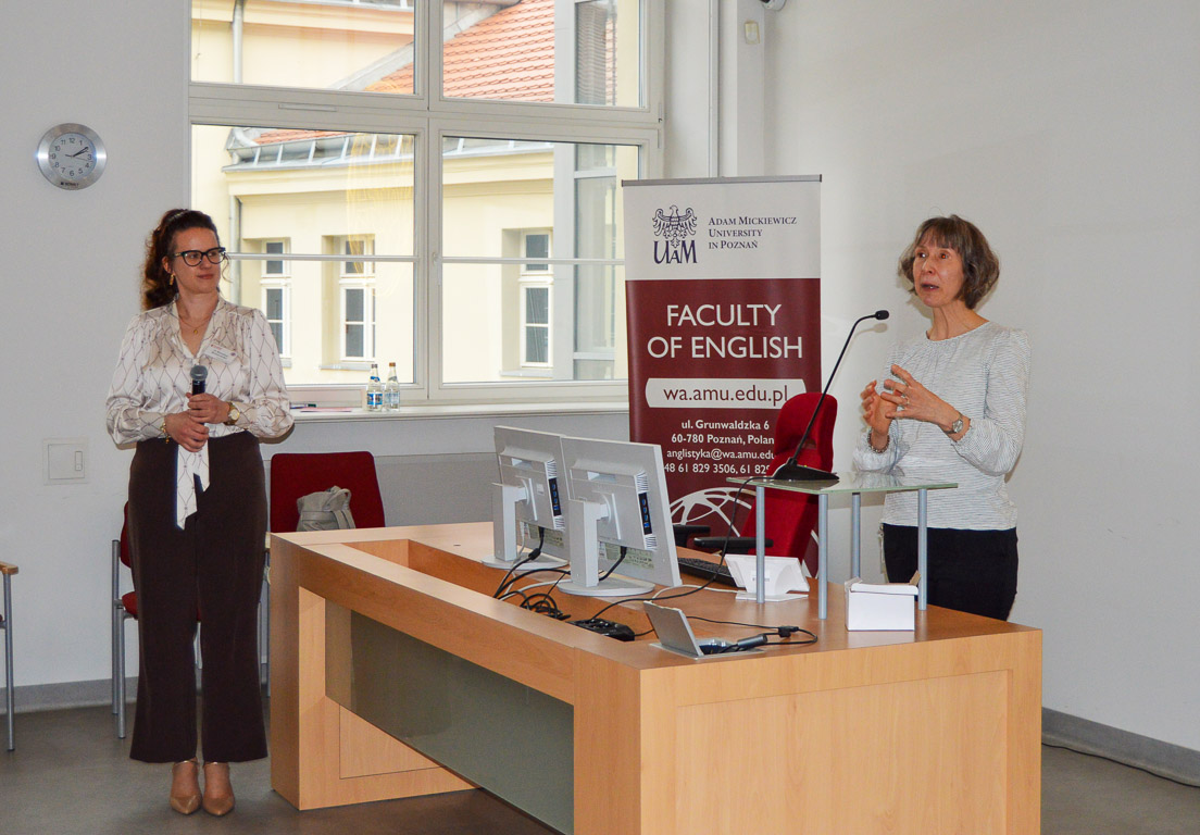 photograph: a person stands behind a table in the lecture hall; the second person, the event moderator, stands further from the table