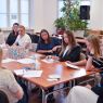 zdjęcie: grupa kilkunastu osób dyskutuje, siedząc wokół połączonych jeden z drugim stołów w sali seminaryjnej