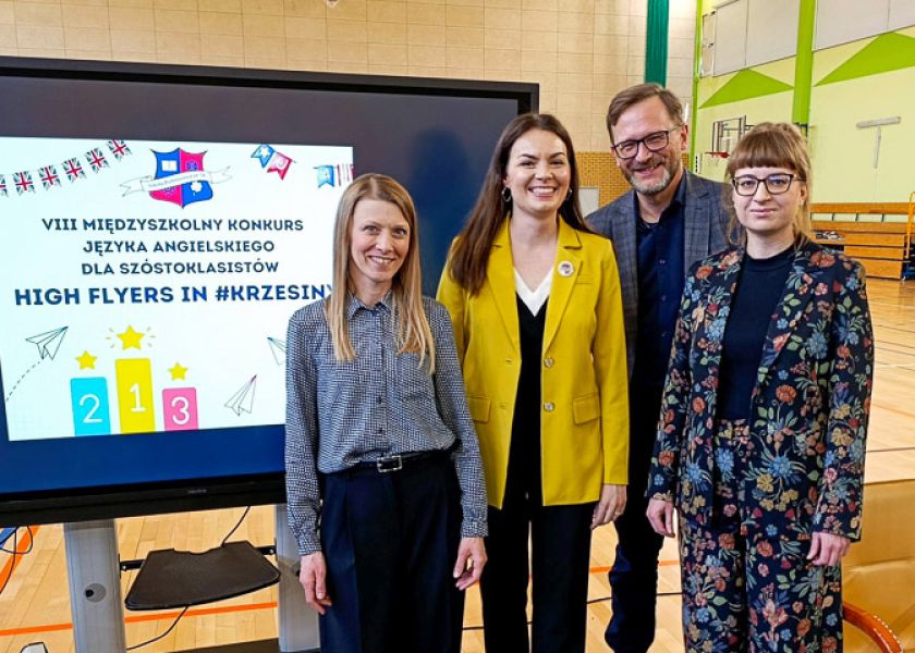 zdjęcie: cztery osoby pozują, stojąc w sali gimnastycznej przy ekranie z wyświetlonym slajdem z prezentacji multimedialnej