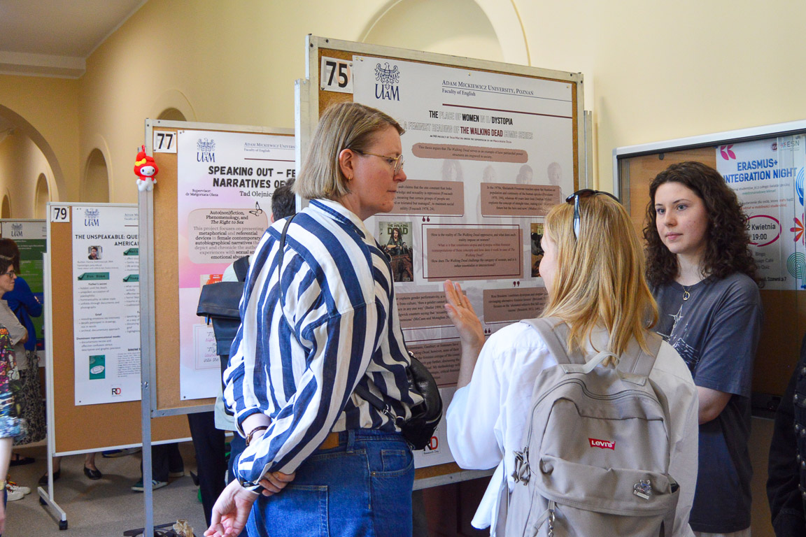 photograph: hallway with conference poster stands, three persons having a discussion by one of such stands