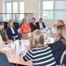 zdjęcie: grupa kilkunastu osób dyskutuje, siedząc wokół połączonych jeden z drugim stołów w sali seminaryjnej