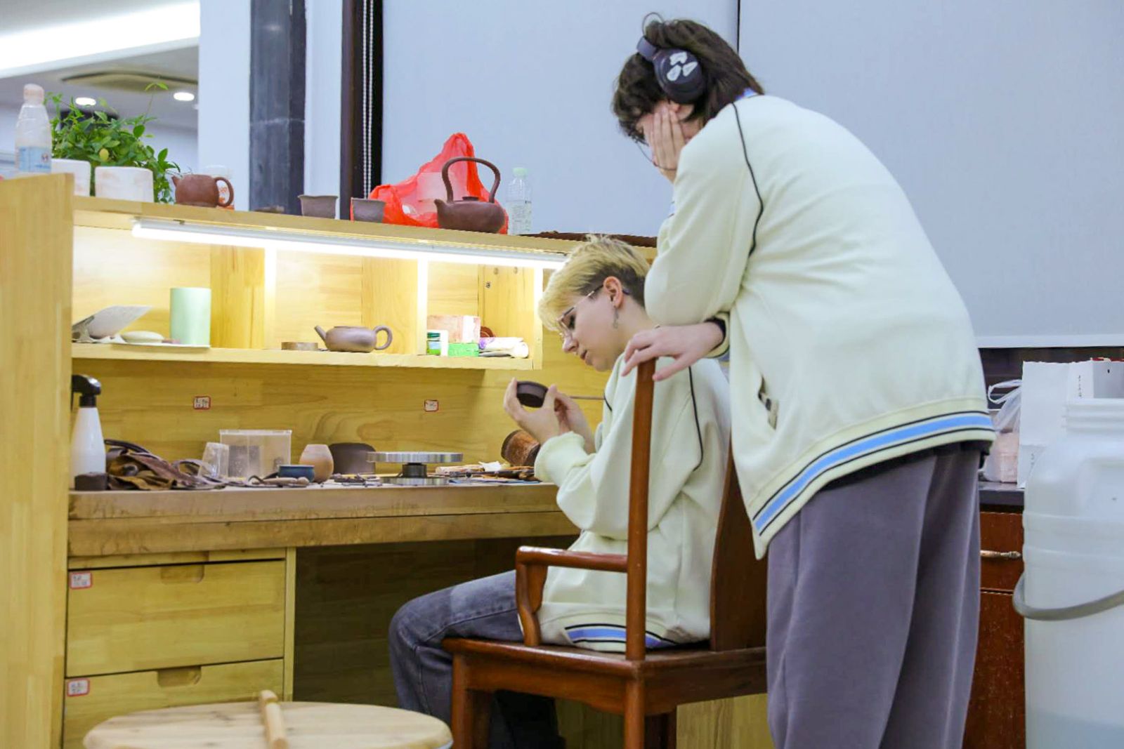 zdjęcie: jedna osoba siedzi, druga osoba stoi przy stole z materiałami garncarskimi