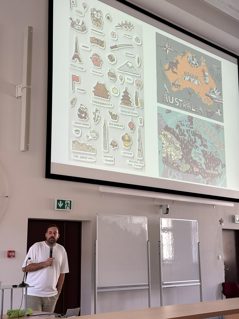 Osoba prowadząca stoi w auli z mikrofonem, omawiając slajd przedstawiający ilustracje i mapy różnych regionów świata.