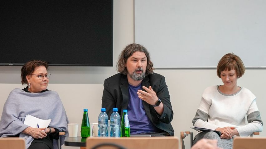 zdjęcie: trzy osoby za stołem, zwrócone do niewidocznej w kadrze publiczności
