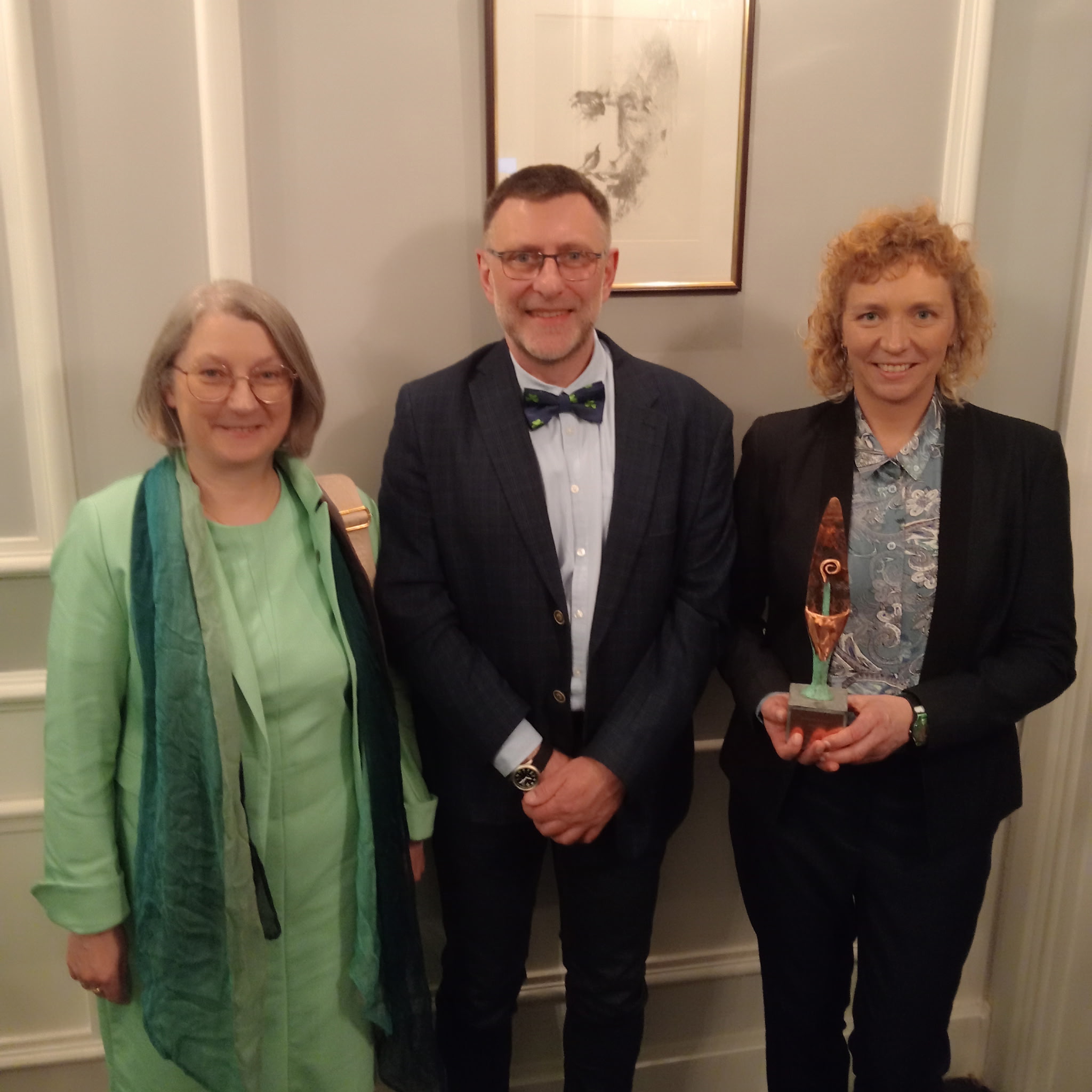 photograph: three persons facing the camera; one of them is holding a statuette