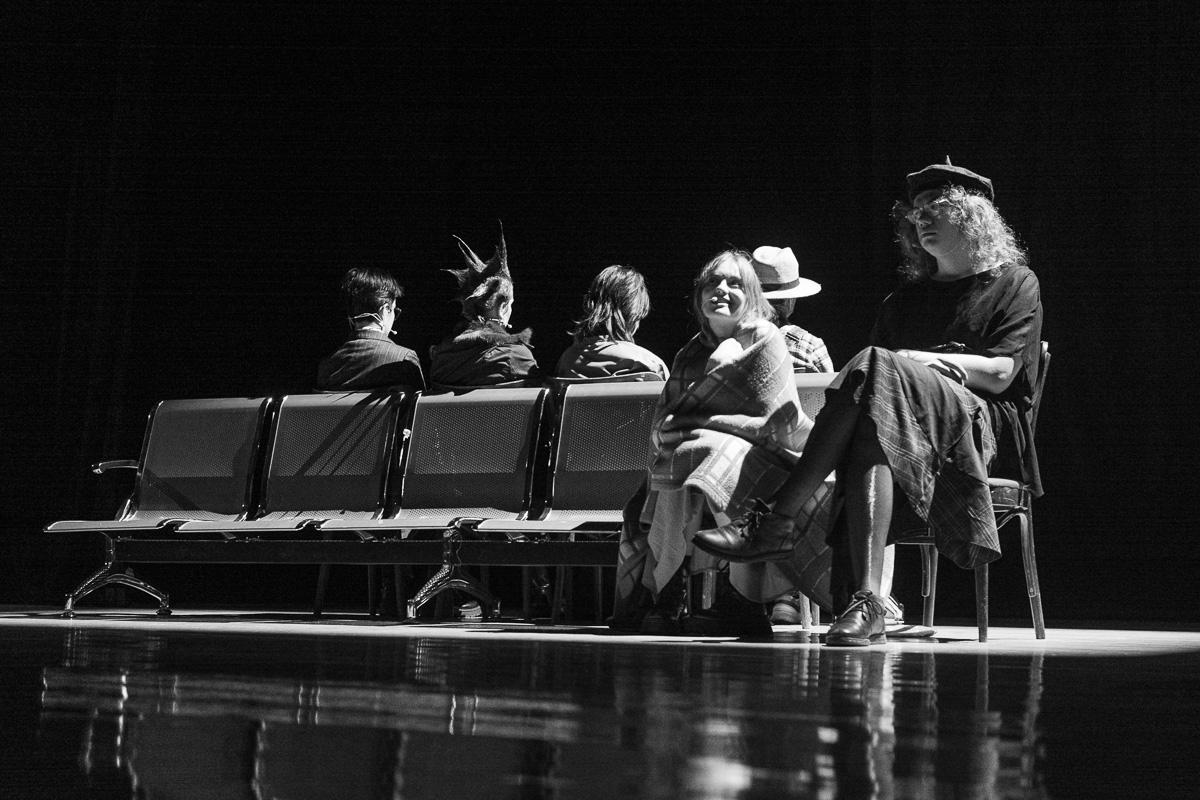 zdjęcie: sześć osób na scenie teatru w trakcie próby spektaklu; cztery siedzą tyłem do kadru, dwie siedzą przodem do kadru