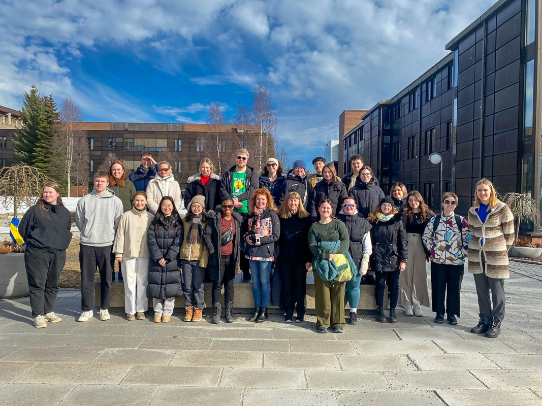 photograph: twenty-six people pose in an open space; some bulidings and a clear sky in the background