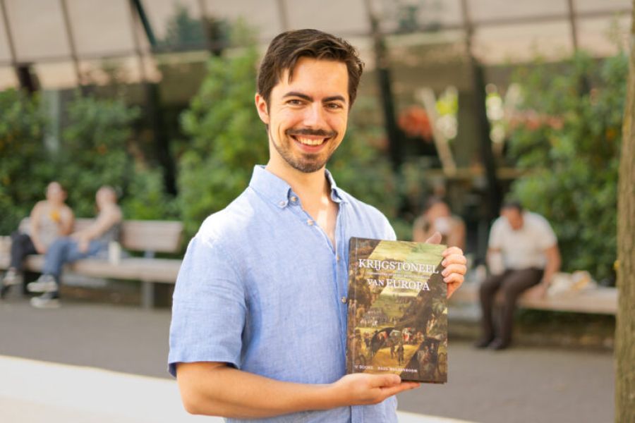 zdjęcie: dr Paul Hulsenboom pozuje z książką swojego autorstwa na tle otwartej przestrzeni rekreacyjnej