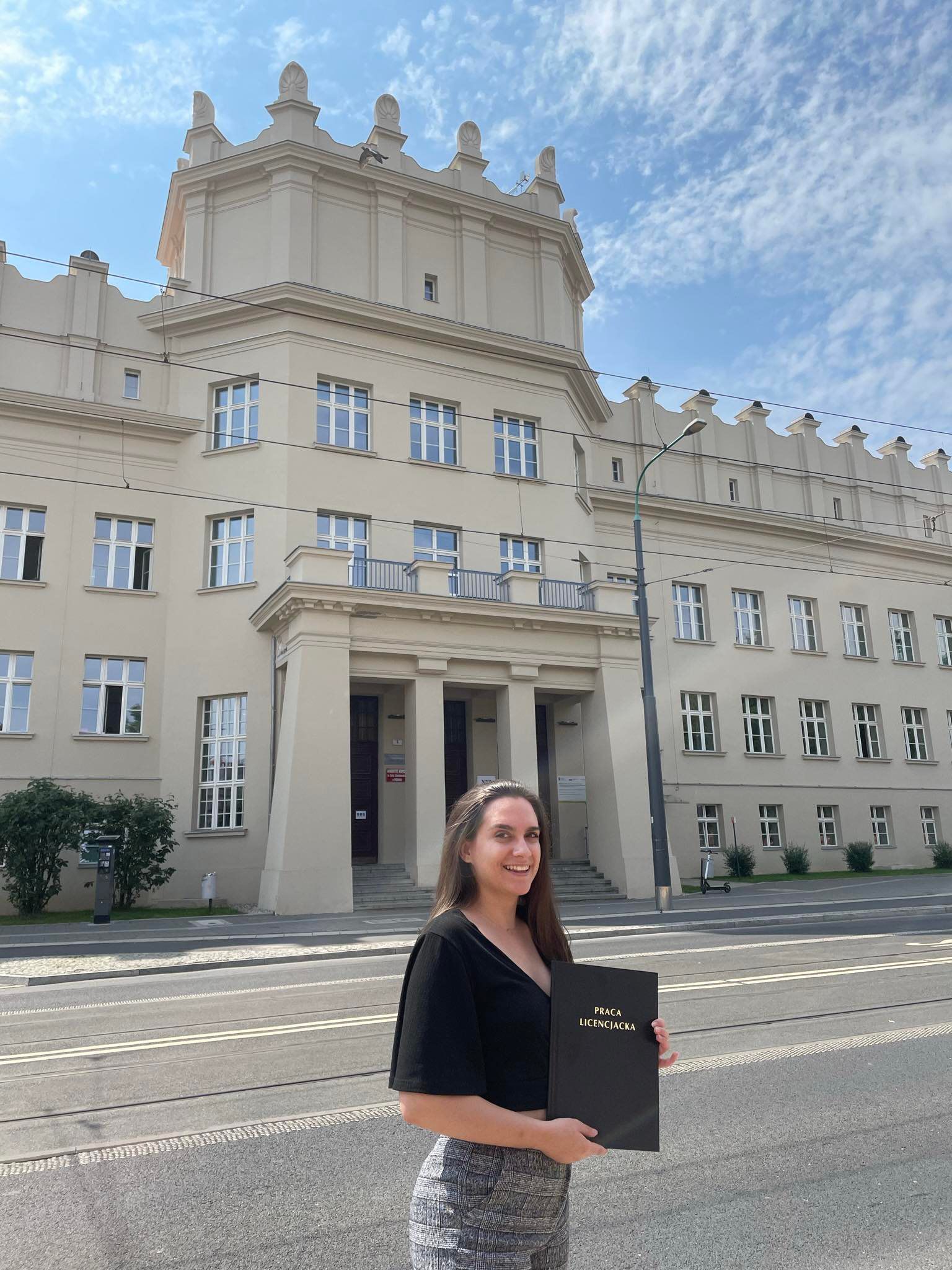 p. Zuzanna Witt przed Collegium Heliodori Święcicki, trzymająca oprawiony egzemplarz swojej pracy dyplomowej