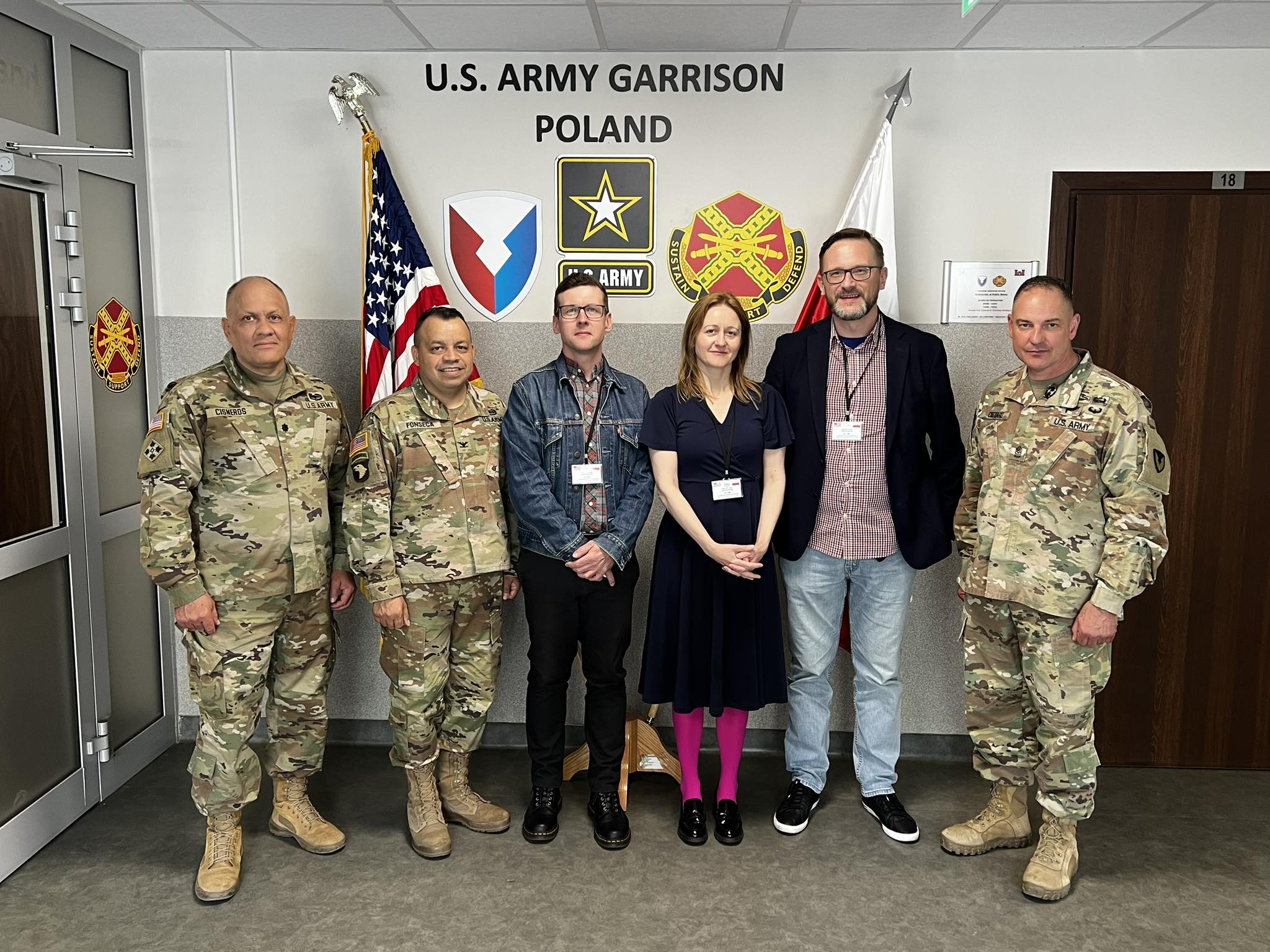 Faculty of English representatives with US Army officers. A text on the wall says U.S. Army Garrison Poland