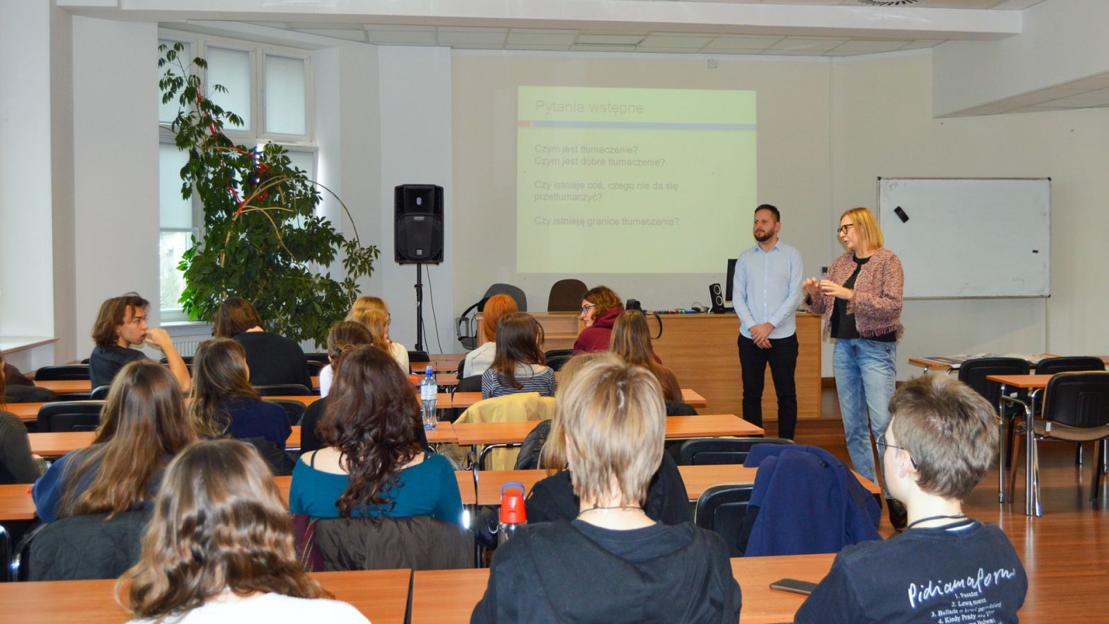 zdjęcie: dwoje prowadzących warsztat lub wykład oraz publiczność w sali seminaryjnej, w tle ekran z obrazem z rzutnika