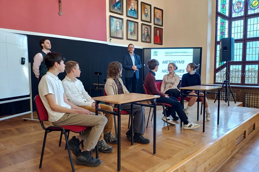 zdjęcie: dwie osoby stoją, sześcioro siedzi przy stołach w sali